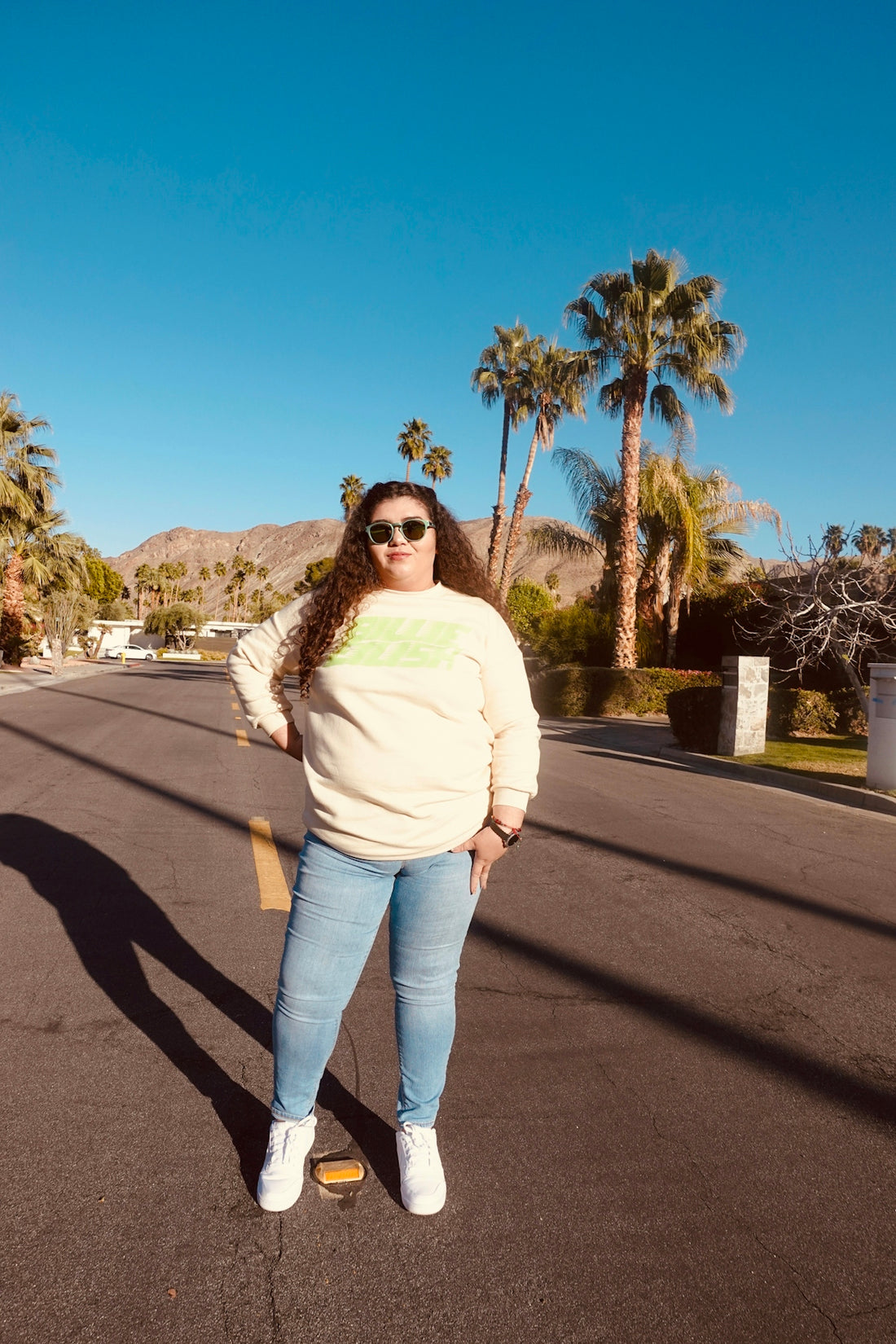 woman in white long sleeve shirt and blue denim jeans standing on gray asphalt road during