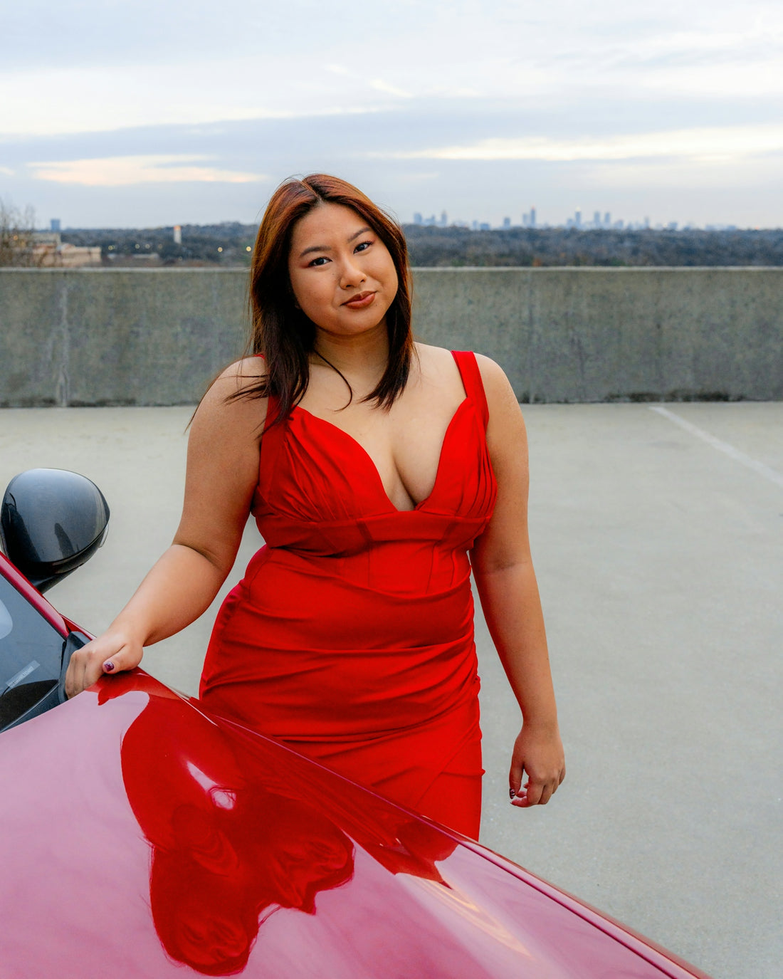 a woman in a red dress leaning on a red car