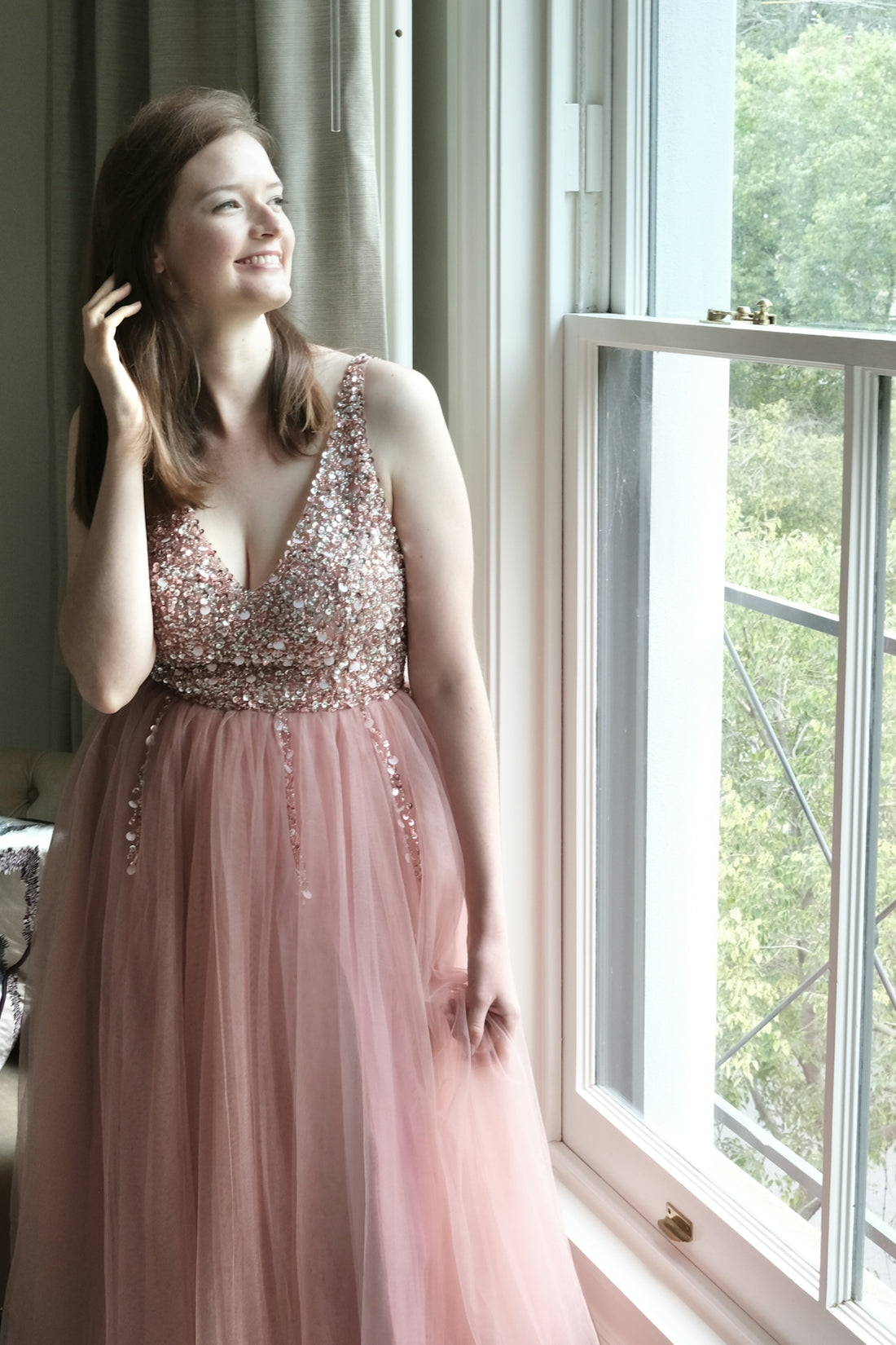 a woman in a pink dress standing next to a window