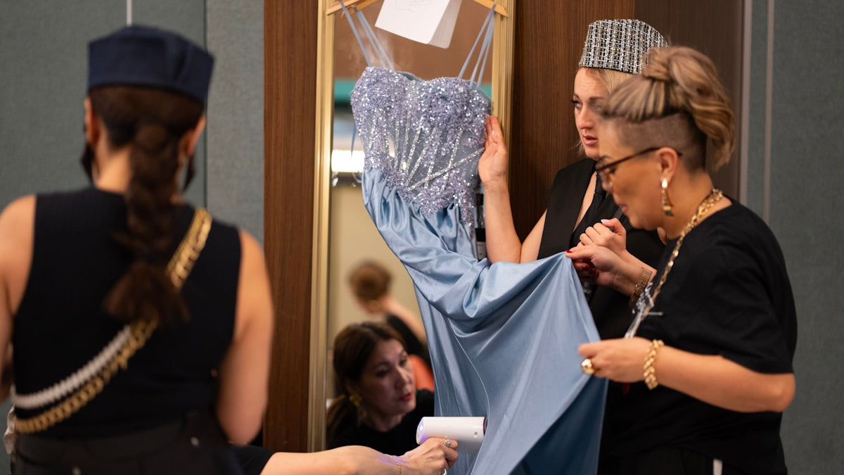 Fashion designers are adjusting a blue dress backstage.
