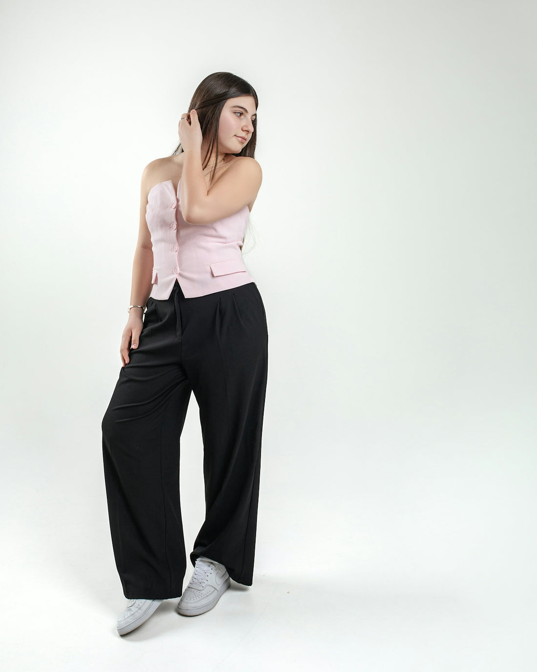 A woman poses in a pink top and black pants.