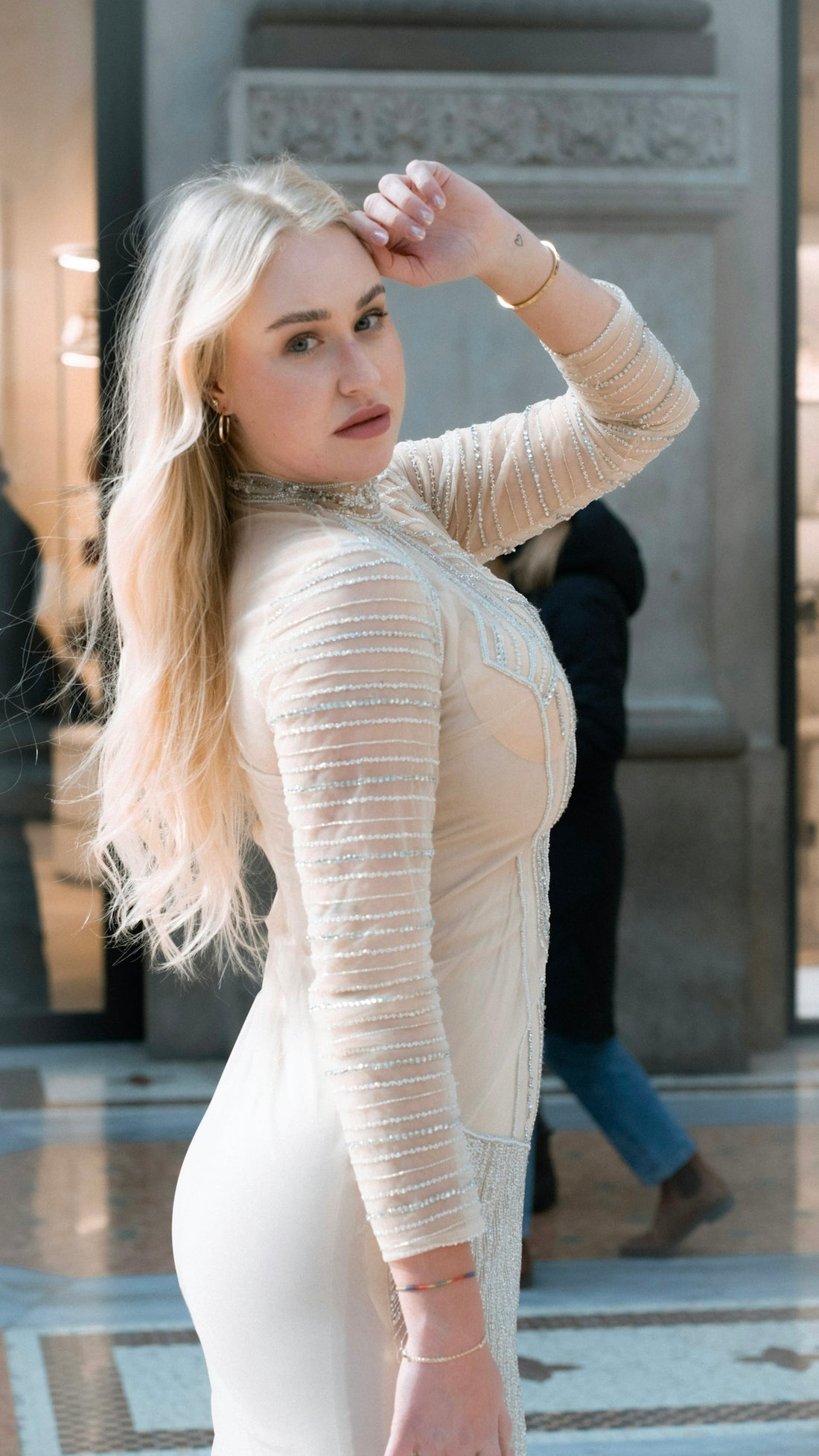 A blonde woman poses elegantly in a beautiful dress.