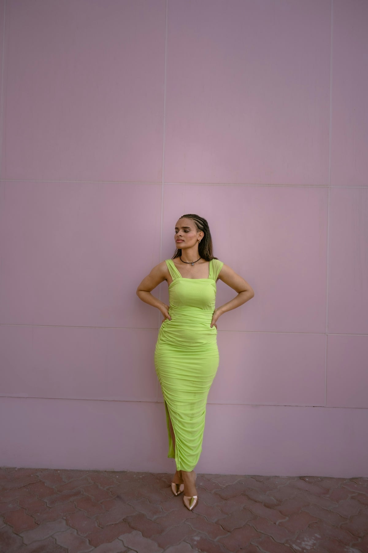 Woman in a neon green dress poses against a pink wall.